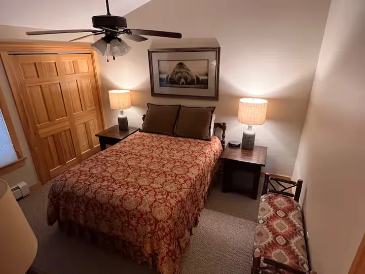 A bedroom with a bed, two nightstands, a ceiling fan, and a picture frame.